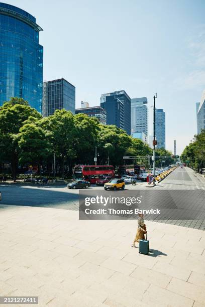 extreme wide shot woman with rolling luggage walking on city boulevard - mexico city building stock pictures, royalty-free photos & images