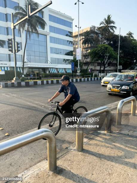 image of indian man cycling on bicycle on main road with taxis and cars in retail district, mumbai, maharashtra, india - chandigarh stock pictures, royalty-free photos & images