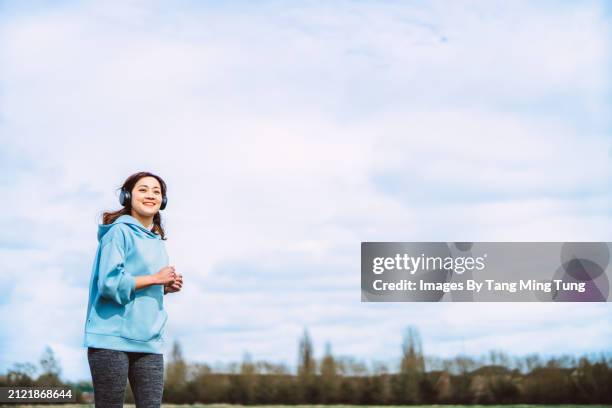 joyful young woman with headphones on a sky-blue morning jog - womens track stock pictures, royalty-free photos & images