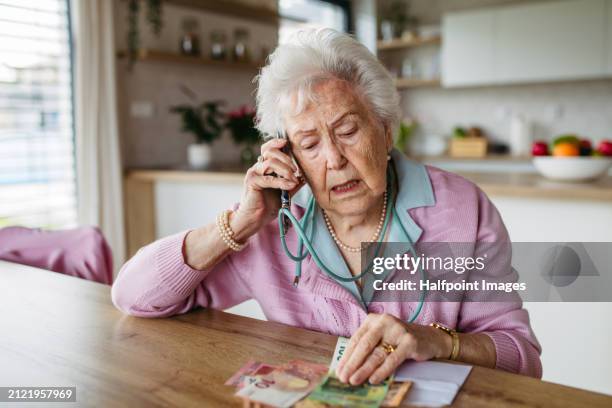 widowed elderly woman with financial problems make phone call. counting money, monthly pension, don’t have enough money for paying utility bills, medication cost, grocery bills. rising food prices as problem for seniors. - widow stock pictures, royalty-free photos & images