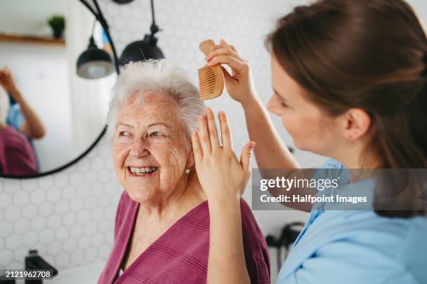 home caregiver helping elderly woman in bathroom, combing her hair. senior woman at home with young beautiful nurse. - kämmen stock-fotos und bilder
