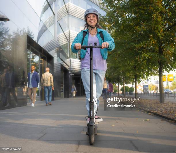 young woman wearing a helmet and riding an e-scooter in the city - helmet stock pictures, royalty-free photos & images