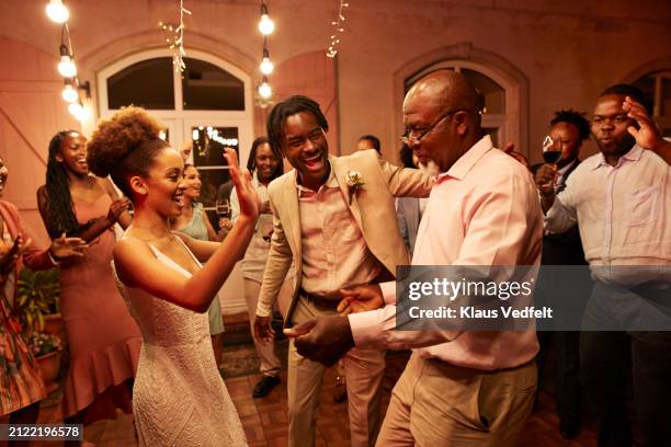 happy senior man dancing with newlywed couple at reception party - wedding first dance stock pictures, royalty-free photos & images