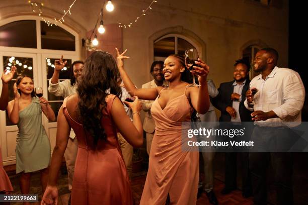 cheerful women with drinks dancing near guests - formell klädsel bildbanksfoton och bilder