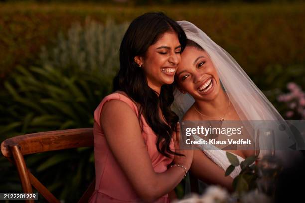 cheerful bride and bridesmaid sitting at table - bruidsmeisje stockfoto's en -beelden