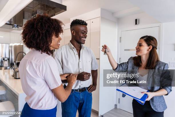 real estate agent giving keys to young couple at home - ethnic millennial real estate stockfoto's en -beelden