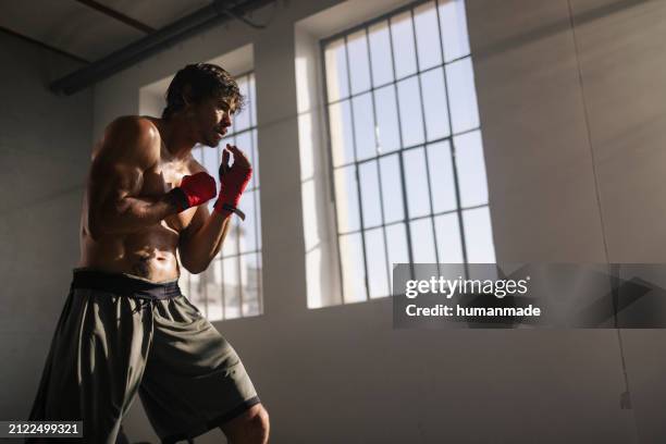 a focused male boxer with hand wraps preparing for a sparring session in a gym, illuminated by natural light from a window. - self-discipline stock pictures, royalty-free photos & images