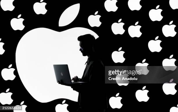 In this photo illustration logos of Apple are displayed on a screen behind a man using macbook in Ankara, Turkiye on March 29, 2024.
