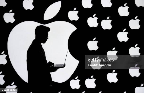 In this photo illustration logos of Apple are displayed on a screen behind a man using macbook in Ankara, Turkiye on March 29, 2024.