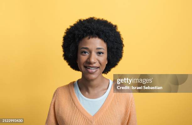 portrait of smiling female in orange sweater looking at camera while standing on yellow background in studio - fashion suit stock pictures, royalty-free photos & images