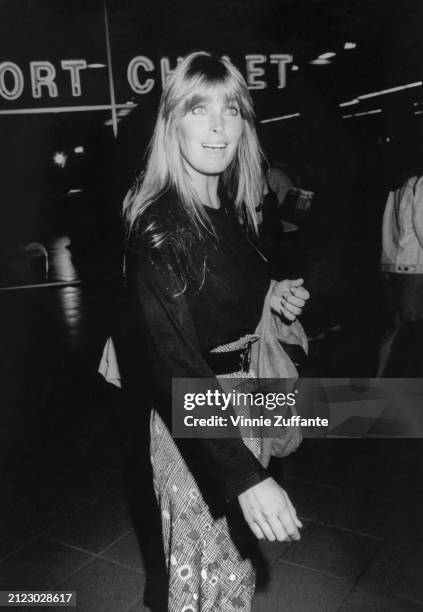 American actress Bo Derek, wearing a black sweater and a patterned skirt, her coat over her arm, attends the Century City premiere of 'Wild at...