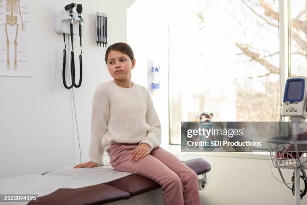 elementary age girl is alone in doctor's examination room - examination table stock pictures, royalty-free photos & images