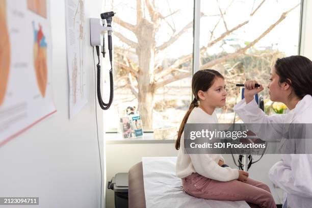 preteen girl sits quietly as female doctor examines eyes - examination table stock pictures, royalty-free photos & images