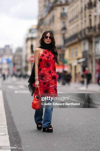 Heart Evangelista wears sunglasses, bracelets, a black scarf, a red floral backless dress, blue denim pants, a red bag, black wedges, outside Akris,...