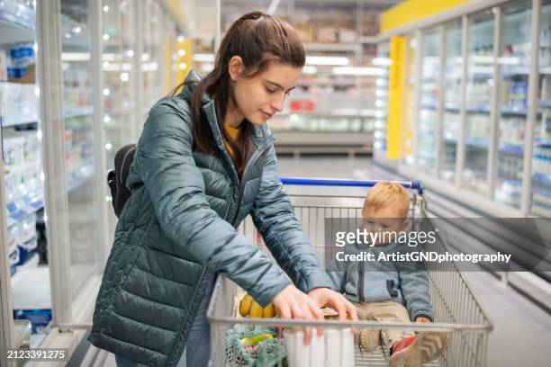 femme faisant ses courses avec son enfant en bas âge au supermarché. - mom buying milk photos et images de collection