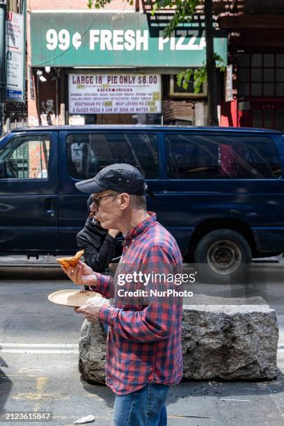 Man is eating a pizza slize. A 99 cent pizza shop with the logo inscription 99c Fresh Pizza, also known as dollar slice in Manhattan, New York City....