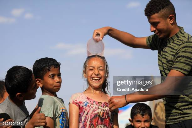 Palestinian children play with water to cool off as people living in makeshift tents try to meet their daily needs as they continue their daily under...
