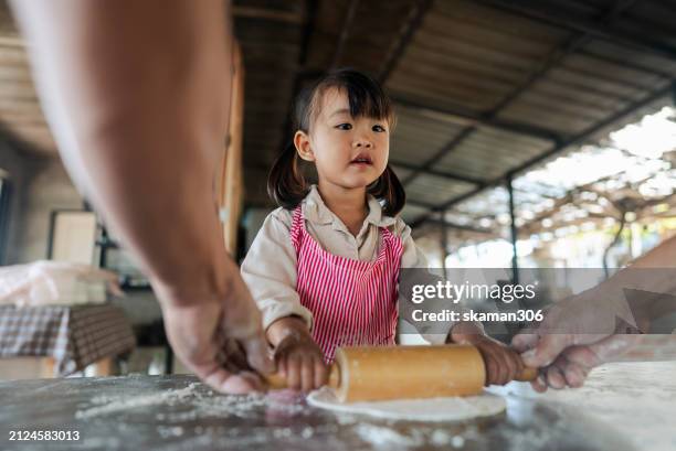 a focused little girl with a rolling pin works on flattening dough in a cooking class, wearing a cute bucket hat and apron. - asian pin up girls stockfoto's en -beelden