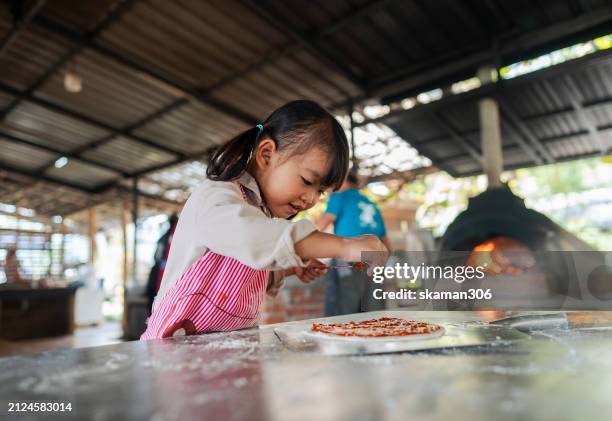 a focused little girl with a rolling pin works on flattening dough in a cooking class, wearing a cute bucket hat and apron. - asian pin up girls stockfoto's en -beelden