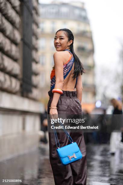 Yuwei Zhangzou wears a orange and blue off-shoulder low-neck top with back nude, burgundy leather pants, a blue Hermes bag, outside Hermes, during...