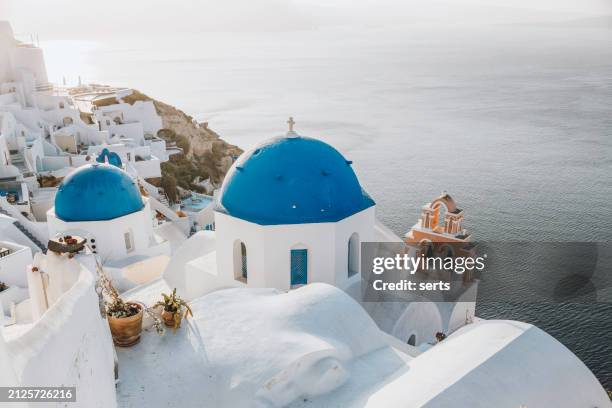 beautiful summer vacation landscape of iconic blue domed churches along the caldera edge at sunny morning after sun rising against clear blue sky in oia, santorini, caldera, greek islands, greece - mediterranean-blue-roof-santorini stock pictures, royalty-free photos & images