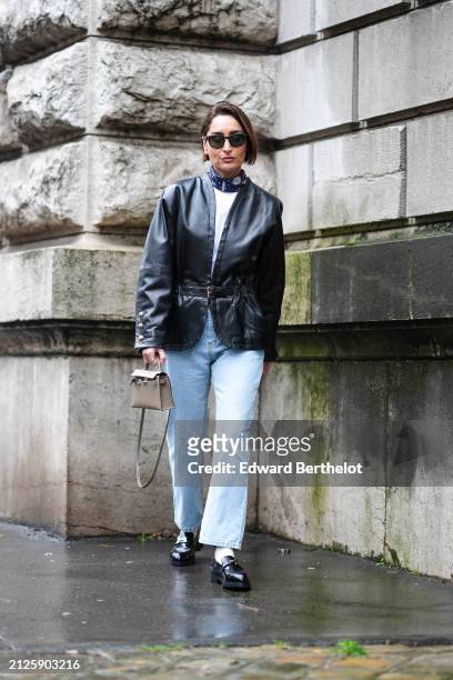 Géraldine Boublil wears a white top, a blue and white scarf, a black leather jacket, blue denim jeans / pants, a beige / brown Hermes Kelly bag,...