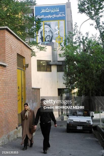 An Iranian couple pass under a huge mural of Khaled Islambouli, who killed Egyptian President Anwar Sadat, on a street named in his honor in Tehran...