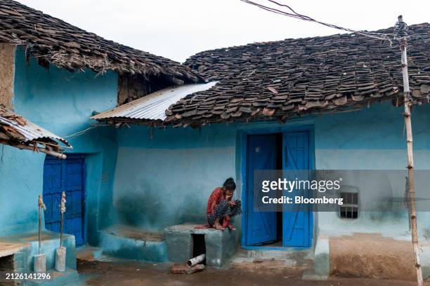 Resident looks at her mobile phone outside her house with a newly installed yet dry water pipe in Naugawan village, in the Banda district of Uttar...