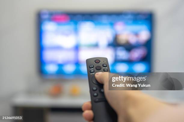 holding a remote control in hand to control a smart tv - multimedia publishing stock pictures, royalty-free photos & images