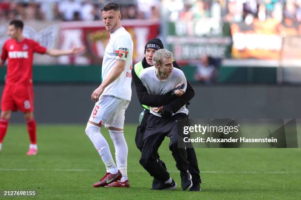 Jeffrey Gouweleeuw of FC Augsburg reacts as a steward stops a pitch invader during the Bundesliga match between FC Augsburg and 1. FC Köln at...