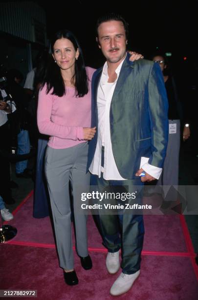 American actress Courteney Cox, wearing a pink sweater and grey trousers, and her husband, American actor David Arquette, who wears a grey suit over...