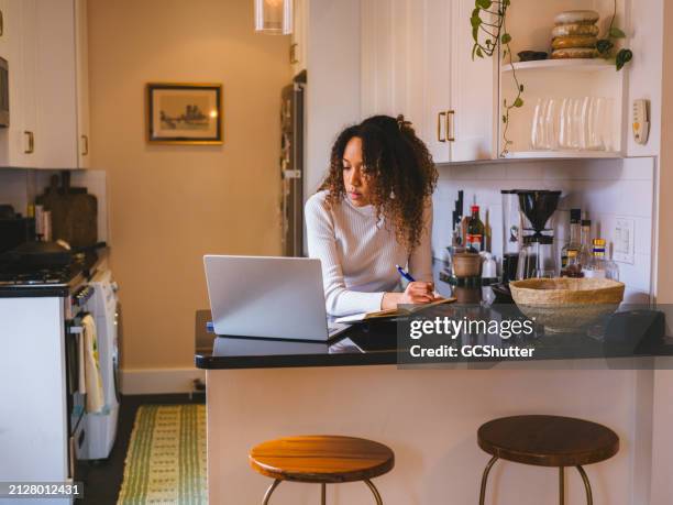 young woman studies in kitchen with laptop and notepad. - studio apartment stock pictures, royalty-free photos & images