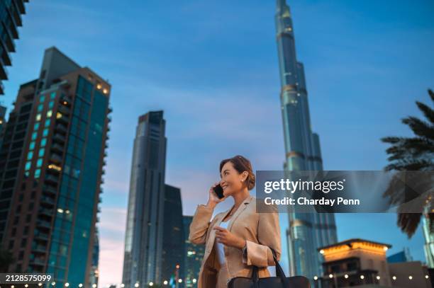 low angle view of smiling asian businesswoman in beige jacket, listening to conversation with client on cellphone in city at night - entrepreneur stockfoto's en -beelden