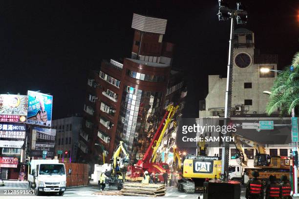 Emergency personnel stand in front of a partially collapsed building leaning over a street in Hualien on April 3 after a major earthquake hit...