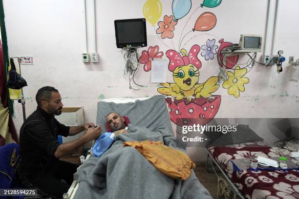 Palestinian man sits on the bedside of a patient in the Children's ward of the Shuhada al-Aqsa Hospital in Deir el-Balah in the central Gaza Strip on...