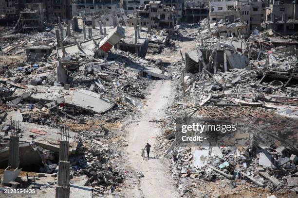 Man pushes a bycicle along as he walks amid building rubble in the devastated area around Gaza's Al-Shifa hospital on April 3 amid the ongoing...