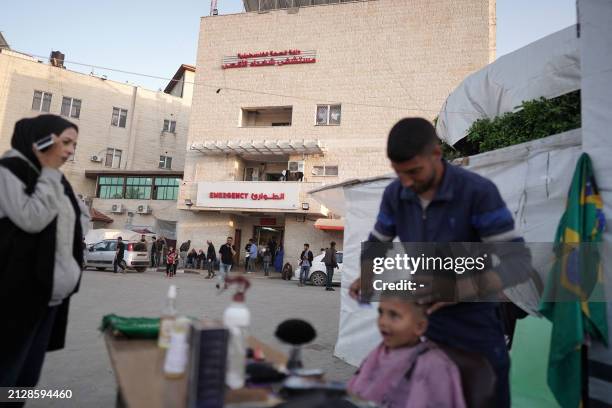 Man gives a young boy a haircut in front of the Shuhada al-Aqsa Hospital in Deir el-Balah in the central Gaza Strip on April 3 amid the ongoing...