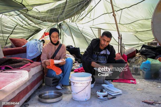 Palestinians perform chores in a makeshift tent made from a parachute used to airdrop food aid, set on the rubble of their home in a devastated area...