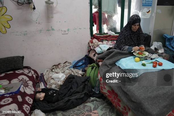 Palestinian woman cuts vegetables near a sleeping boy at the Shuhada al-Aqsa Hospital in Deir el-Balah in the central Gaza Strip on April 3 amid the...