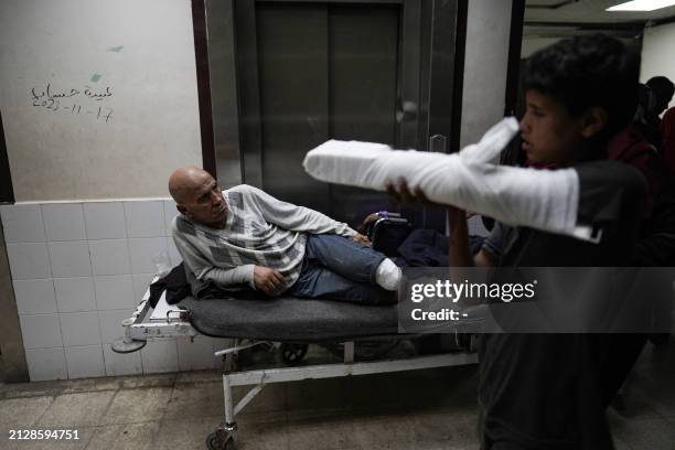 An injured boy walks near an amputated Palestinian man lying in the corridor at the Shuhada al-Aqsa Hospital in Deir el-Balah in the central Gaza...