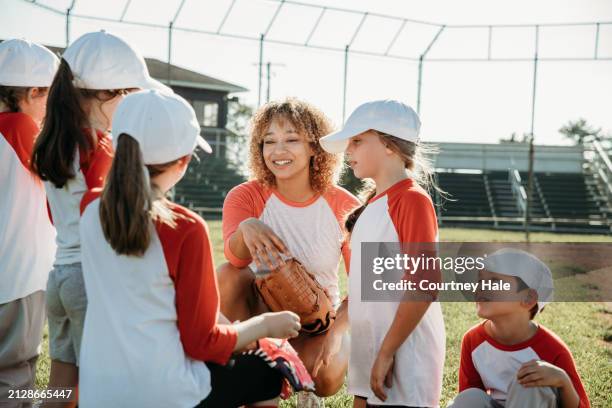 gecoacht und angeleitet kommen die sportler der grundschule in einem gemischten baseballteam der kleinen liga zusammen, das auf einem ballfeld spielt - außerschulische aktivität stock-fotos und bilder