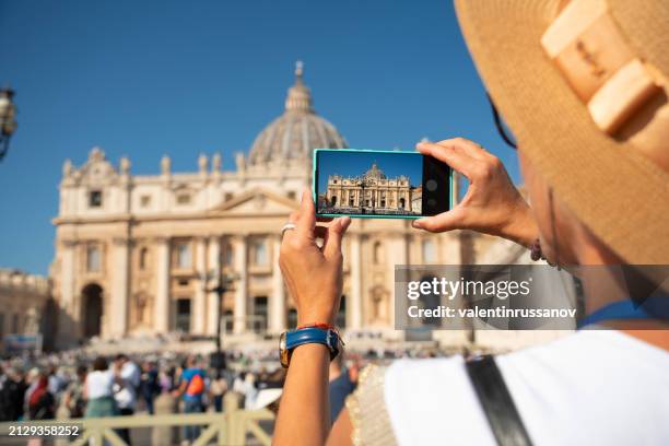women takes a photo with a smartphone of the st. peter's basilica in vatican city, rome, italy - romeinse rijk stockfoto's en -beelden