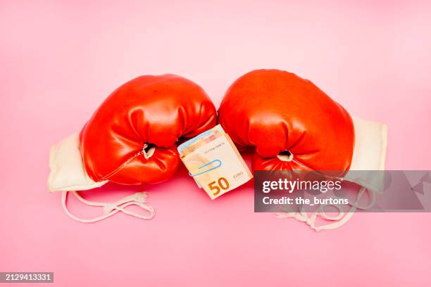pair of red boxing gloves and bundle of euro banknotes on pink background - money box foto e immagini stock