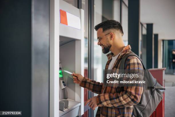 adult young man using a street atm machine and withdrawing money. - geldautomaat stockfoto's en -beelden
