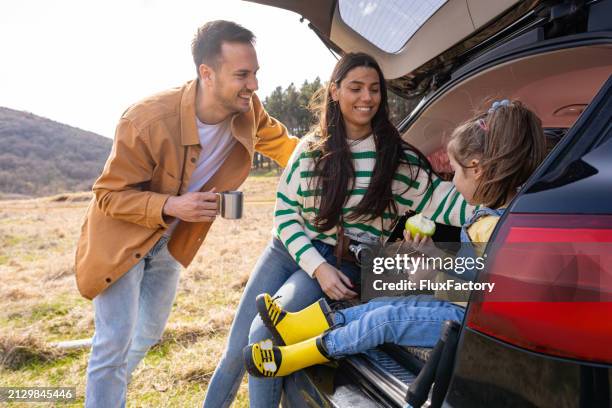 girl having apple for a snack, while her parents drinking coffee while resting from a hike - car snacks stock pictures, royalty-free photos & images