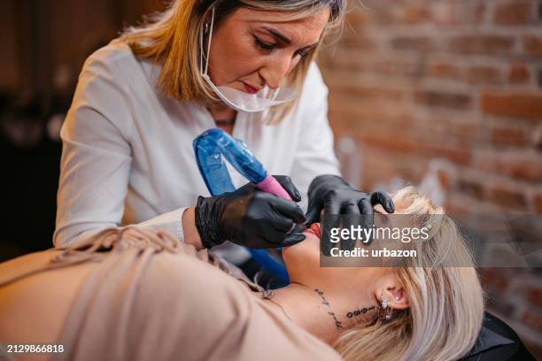 female beautician tattooing her client's lips at a beauty salon - lip tattooing stock pictures, royalty-free photos & images