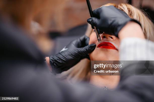 female beautician tattooing her client's lips at a beauty salon - lip tattooing stock pictures, royalty-free photos & images