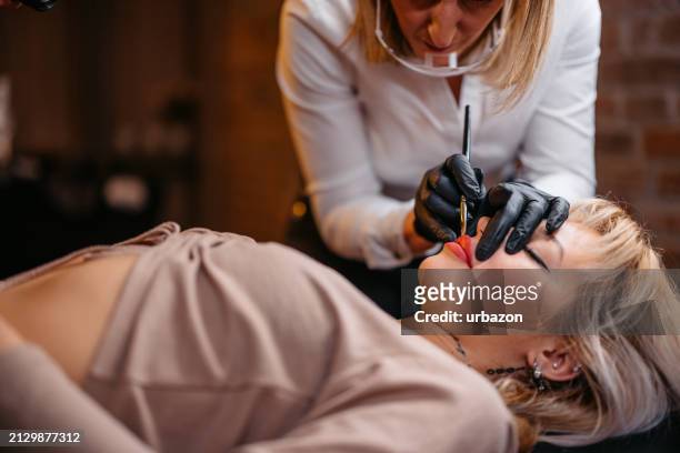 female beautician tattooing her client's lips at a beauty salon - lip tattooing stock pictures, royalty-free photos & images
