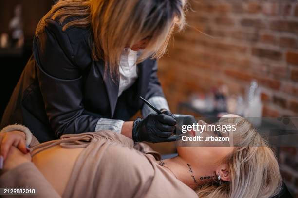 female beautician tattooing her client's lips at a beauty salon - lip tattooing stock pictures, royalty-free photos & images