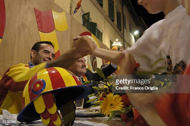 People greet a rider during a dinner on a street of the Chiocciola's Contrada, one of the ten Siena districts, following the "Palio di Siena" July 1,...